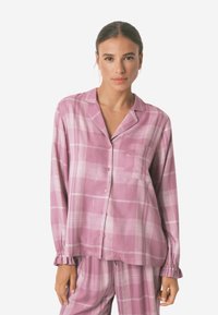 Pink ternet pyjamasæt lavet af blødt stof, der har en pæne skjorte med lange ærmer og matchende bukser, begge med rynkede ærmer.