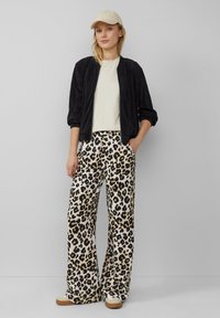 Černá ribbed bomber bunda, krémové tričko a volné leopardí kalhoty. Světle hnědé tenisky. Svetlý klobouk dotváří outfit.