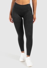 Zwarte high-waisted leggings van zachte stof met een geribde tailleband en textuuraccenten op de dijen, gecombineerd met witte sneakers.