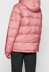 Różowa kurtka puchowa z kapturem, z pikowanym wzorem i ściągaczami na rękawach. Na lewym ramieniu znajduje się okrągła naszywka z logo.