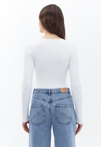 Witte lange mouw bodysuit gecombineerd met lichtblauwe high-waisted denim jeans met een gestructureerde afwerking en een achterpatch met het merkje.