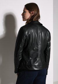 Veste de moto en cuir noir avec un design ajusté, des accents matelassés sur les épaules et des poignets zippés. Texture lisse, matériel minimal.