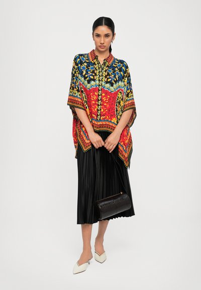 Colorful patterned kimono with red, blue, and yellow tones, featuring an intricate design. Black pleated skirt and brown handbag complete the look.