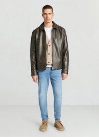 Veste en cuir marron avec col à revers, fermeture éclair et deux poches avant, portée sur un cardigan beige et un jean bleu clair.