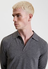 Graues langärmeliges Poloshirt mit weichem Material, drei Knöpfen und klassischem Kragendesign. Keine sichtbaren Muster oder Akzente.