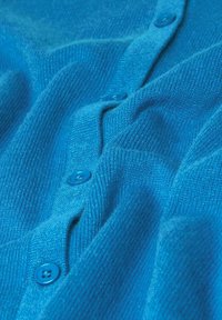 Strick blauer Cardigan mit glatter Textur, einer Reihe passender blauer Knöpfe und einem dezenten Rippmuster entlang des Stoffes.