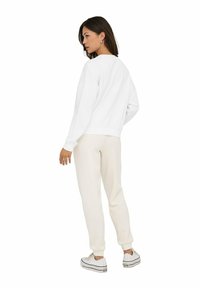 Witte crew-neck sweatshirt met verlaagde schouders, gecombineerd met lichtbeige joggers en witte sneakers. Glad textuur, casual pasvorm.