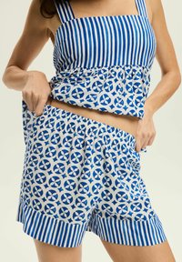 Niebiesko-biała krótka bluzka z pionowymi paskami i kwiatowym wykończeniem. Pasujące szorty mają elastyczny pas i podobny wzór.