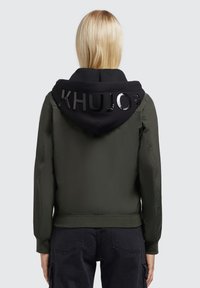 Maslinasto zelena bomber jakna s crnom kapuljačom. Kapuljača ima hrabro, sjajno "KHUJO" natpis. Glatka tkanina, rebrasti manžete i donji rub.