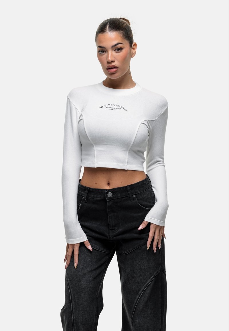 Weißes Langarm-Crop-Top mit geripptem Textur und Details, kombiniert mit hoch taillierten schwarzen Jeanshose mit einzigartigen Nahtmustern.