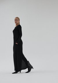 Czarna sukienka na długi rękaw o dopasowanym kroju, z bocznymi rozcięciami i teksturowaną tkaniną, zestawiona ze spiczastymi czarnymi botkami. Minimalistyczny design.