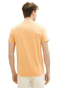Kortærmet t-shirt med rund hals i lys orange bomuldsstof. Har en glat tekstur med en afslappet pasform og dobbelt syninger i kanten.