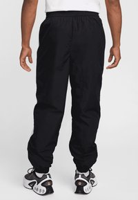 Pantalones deportivos negros con cintura elástica, piernas ajustadas y una textura suave, que cuentan con franjas laterales y puños en los tobillos.