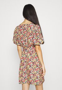Blumenkleid mit gelbem Grund, verziert mit pinken, blauen und roten Blumen. Kurze Puffärmel und taillierte Taille, mit schwingendem Saum.