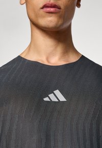 Musta tekninen t-paita, jossa on teksturoitu kuvio ja pyöreä pääntie. Rintakehässä valkoinen logo, valmistettu kevyestä materiaalista.