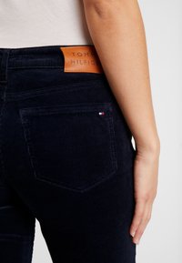 Navy corduroy-housut, joissa on tekstuuri. Varustettu nahkasta valmistetulla logo-tarralla vyötäröllä ja pienellä brodeeratulla lippuyksityiskohdalla takataskussa.