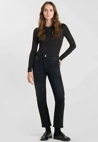 Svart långärmad topp kombinerad med mörka denimjeans. Jeansen har raka ben, fem fickor och knappstängning framtill.