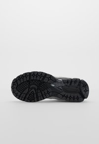 Semelle d'une chaussure de sport noire avec un motif de bande de roulement texturé pour l'adhérence, présentée sur un fond uni clair.