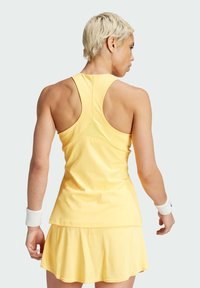 Top atletico senza maniche giallo con scollatura rotonda, design a spalle scoperte e apertura sul retro. Accompagnato da una gonna plissettata gialla.