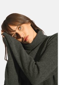 Ciemnoszary sweter z wysokim golfem, z długimi, rozszerzanymi rękawami i miękkim, teksturowanym splotem. Prosty i przytulny design.