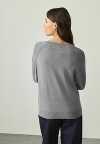 Grå sweater med en afslappet pasform, blød tekstur, raglanærmer og ribbede kanter ved hals og nederste kant, parret med mørke bukser.