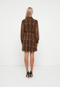 Brun leopardmønstret kjole med lange ermer og innsvingt midje. Gjennomsiktig materiale, lengde over kneet, kombinert med svarte høye hæler.