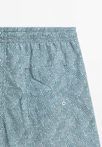 Shorts bleu à motifs avec une taille élastique, dotés d'une poche à rabat et de lignes en zigzag blanches sur un tissu texturé.