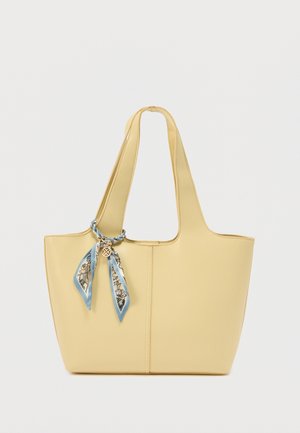 Borsa tote beige con manici larghi e una sciarpa decorativa blu e bianca legata a una delle maniglie.