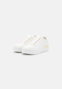Baskets blanches avec une tige texturée, bout rond, semelle plate blanche et accent doré sur le côté, comportant six œillets pour les lacets.
