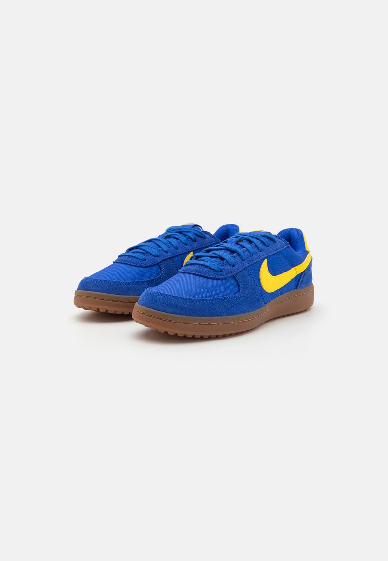 Zapatillas de ante azul y malla con acentos amarillos, diseño con cordones y suela de goma marrón; puntera redondeada y detalles en la superficie texturizados.