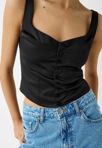 Czarny satynowy krótki top z szerokimi ramiączkami, kwadratowym dekoltem i centralnym zapięciem na guziki. Połączony z jasnoniebieskimi szortami dżinsowymi z wysokim stanem.