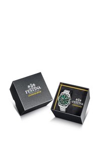 Sudraba nerūsējošā tērauda pulkstenis ar zaļu ciparnīcu, pasniegts melnā tekstūrētā kastē. Kastei ir zelta un baltas krāsas zīmējums.