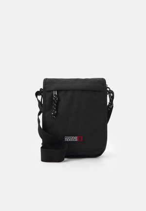 Bolso cruzado negro hecho de tela duradera, con cierre de solapa, correa ajustable y un parche de logo en colores contrastantes.