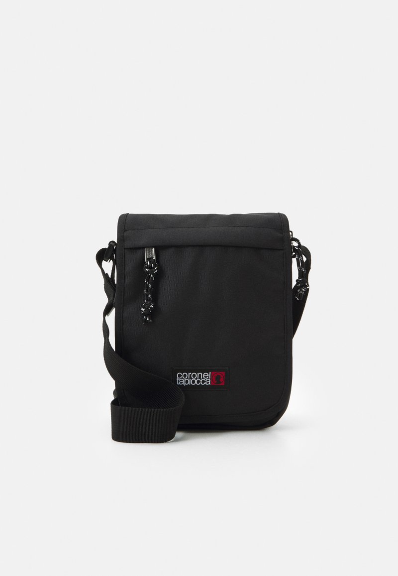 Bolso cruzado negro hecho de tela duradera, con cierre de solapa, correa ajustable y un parche de logo en colores contrastantes.