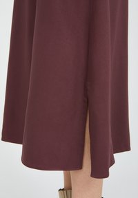 Middihame maroon pehmeästä kankaasta, jossa on sivureikä. Hameessa on huoliteltu helma ja sileä rakenne. Yksinkertainen muotoilu ilman näkyviä kuvioita.