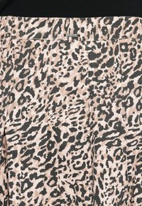 Jupe imprimée léopard en tissu texturé beige et noir, avec une étiquette logo visible à la taille et des éléments de design plissés.