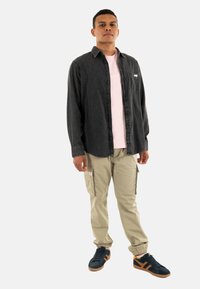 Conjunto informal compuesto por una camisa de mezclilla negra con botones, camiseta rosa, pantalones cargo caqui con bolsillos y zapatillas negras con acentos naranjas.