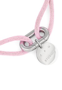 Collana con cordino intrecciato rosa, dotata di chiusura in metallo argentato e un ciondolo rotondo inciso con "C P H STUDIOS."