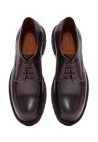 Zapatos de piel marrón con una textura suave, punta redonda y cordones tradicionales. Presentan un diseño cosido y una suela Texturizada para mayor agarre.
