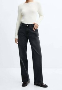 Mustat leveälahkeiset farkut korkealla vyötäröllä ja näkyvillä saumoilla, yhdistetty valkoiseen ribbineulottuun pitkähihainen paitaan. Sileä puuvillasekoitemateriaali.