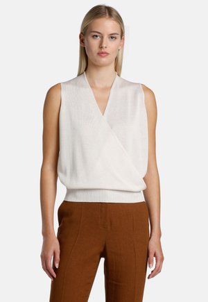 Sleeveless cream top with a deep V-neck, wrap design, and a gathered waistband. Soft texture with a slight sheen, paired with brown pants.