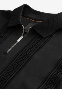 Černé polo triko na zip s texturovaným límcem, který má na přední straně reliéfní vzor řeckého klíče a kovový zip.