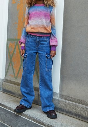 Mønstret striktrøje i flere farver med en gradient af pink, orange og blå; blå cargo-bukser med sidelommer og en løs pasform; mørke platform-sko.