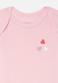 Lyserosa bomullsheldrakt med rund halslinning. Har tre små hjerter i rød, lavendel og hvit på brystområdet.