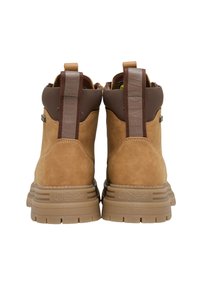 Bottes cheville en daim beige avec accents en caoutchouc marron, dotées d'une semelle robuste, de talons renforcés et de détails de logo sur les languettes de talon.