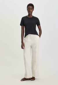 Zwarte shirt met korte mouwen gecombineerd met crèmekleurige wijde broek en bruine sandalen. De outfit heeft eenvoudige, strakke lijnen en een relaxte pasvorm.