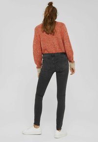 Svarta slim fit jeans med hög midja, ihop med en röd stickad tröja med beige manschetter, bärs med vita sneakers.