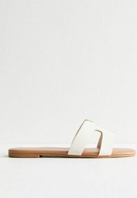 Witte neplederen slip-on sandaal met een uitsnijdesign, platte tan kleurige zool, gladde textuur en een minimalistische, moderne esthetiek.