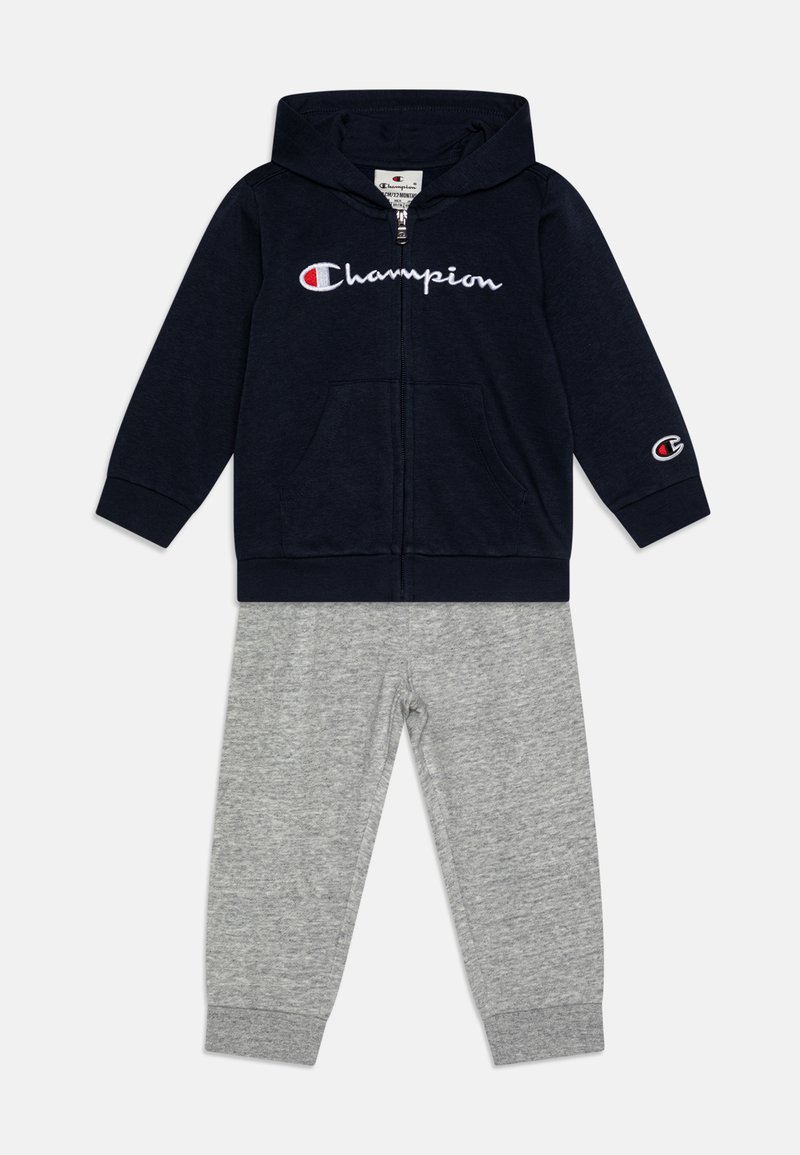 Sudadera con cremallera en color azul marino con el logo blanco de "Champion" y pantalones de chándal grises, confeccionados en mezcla de algodón, con puños de canalé y bolsillos laterales.