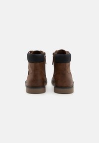 Botas de piel marrón hasta el tobillo con un cuello de tela negra, que presentan una textura suave, cremalleras laterales y un tacón bajo de goma.